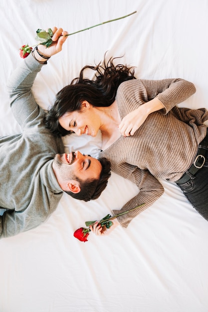 Cheerful couple with roses on white sheet