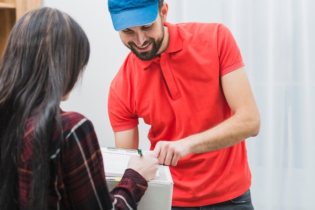 Cheerful courier pointing to clipboard for woman