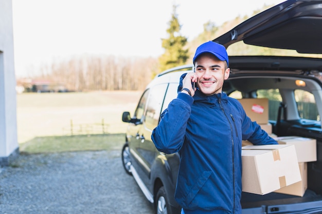 Cheerful courier with box talking on phone