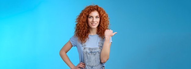 Free photo cheerful curious lively redhead goodlooking curlyhaired girl wearing summer overalls tshirt pointing