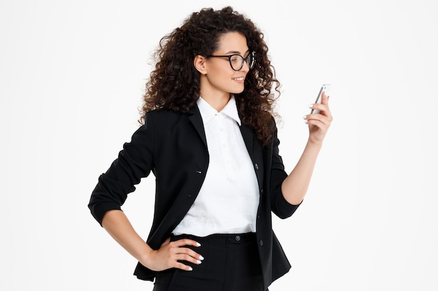  cheerful curly business girl wearing glasses looking at phone