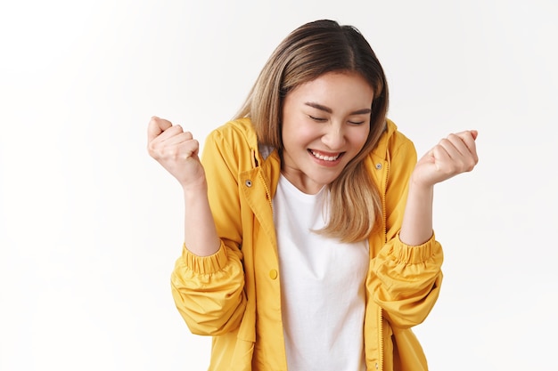 Ragazza bionda asiatica carina allegra sentirsi felicissima felicità dolce successo ballare chiudere gli occhi sorridere ampiamente stringere le mani trionfante celebrare la vittoria notizie eccellenti punteggio perfetto raggiungere l'obiettivo