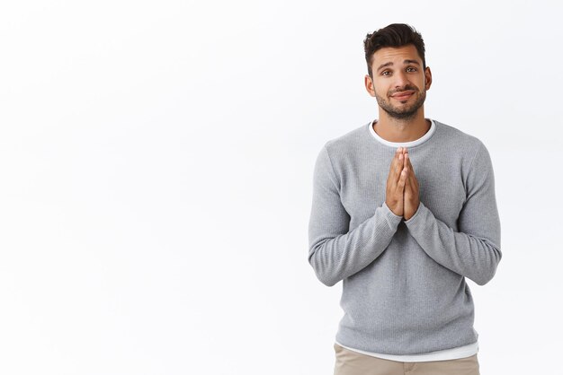 Cheerful cute goodlooking bearded boyfriend making promise or asking offer hold hands in pray press palms together over chest smiling cute need something want advice white background