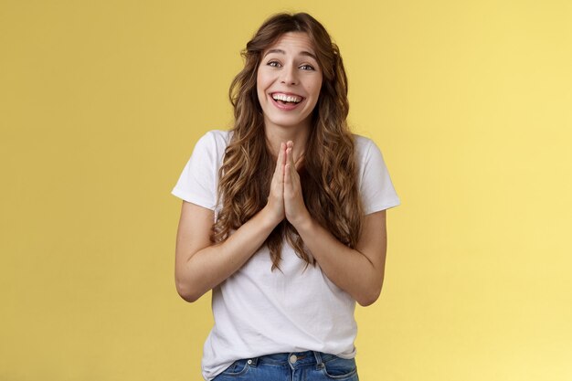 Cheerful cute hopeful girl clingy begging look camera optimistic faithfully press palms together pray supplication gesture asking favour pleading apology positive lucky mood yellow background