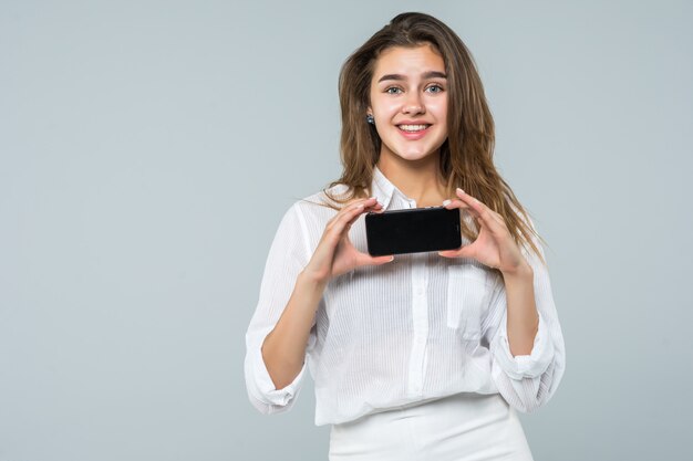 Cheerful cute woman pointing finger on smartphone screen isolated on a white background.