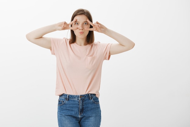 Allegra donna carina che mostra gesti di pace, kawaii in piedi sopra il muro bianco