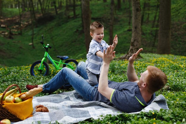 Cheerful dad and son have fun playing on the plaid in a green park