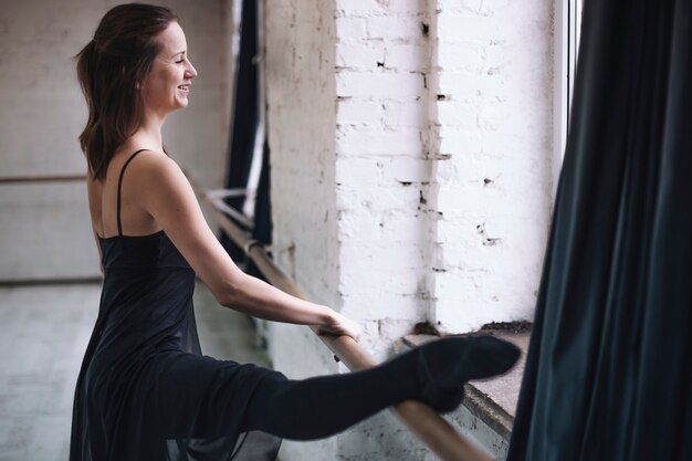 Cheerful dancer stretching leg on barre