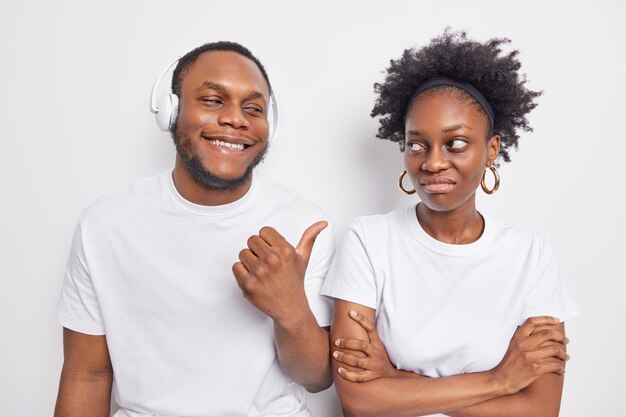 Cheerful dark skinned guy points at offended female friend 