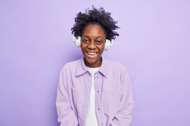 Жизнерадостная смуглая девочка-подросток с удовольствием слушает музыкальные улыбки, используя беспроводные наушники.