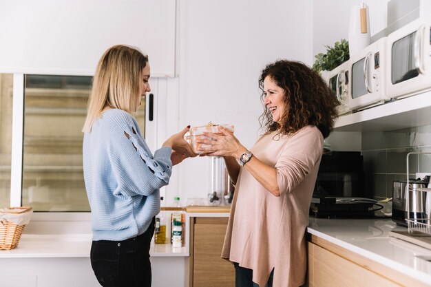 Cheerful daughter giving gift to mother in kitchen