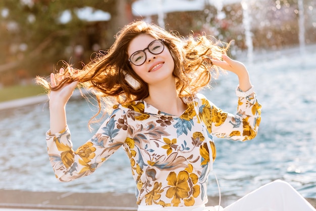 Cheerful elegant lady playing with her curly hair and enjoying life in sunny day