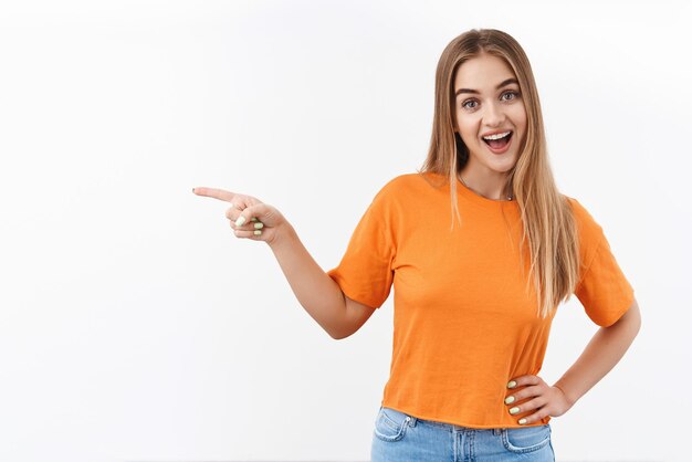 Cheerful enthusiastic blonde girl pointing finger left, smiling excited