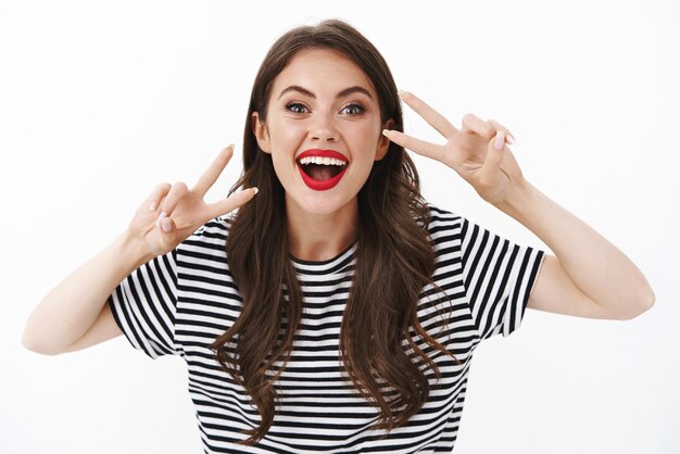 Cheerful enthusiastic happy woman red lipstick, striped t-shirt, having fun, enjoy awesome tourist travel show peace, victory sign joyfully posing