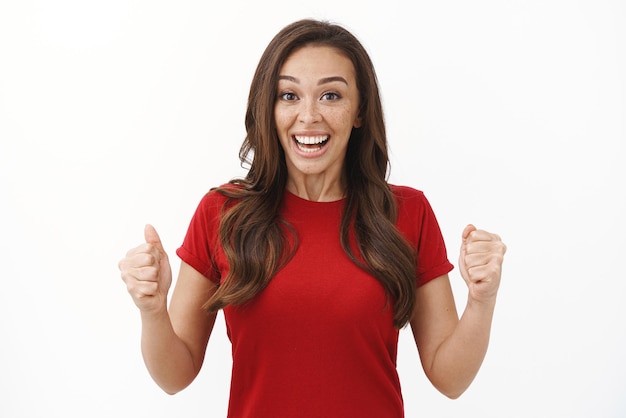 Cheerful enthusiastic young brunette female in red tshirt rooting for friend fist pump smiling accomplished achieve success winning competition feel happy receive award triumphing joyfully