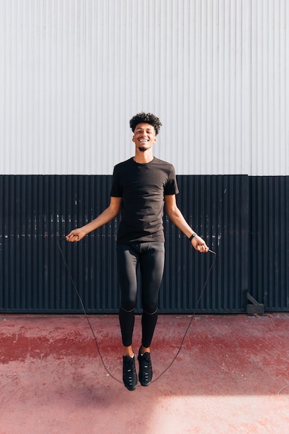 Cheerful ethnic athletic guy jumping rope