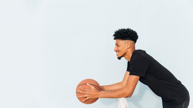 Cheerful ethnic male leaning on fence holding basketball 