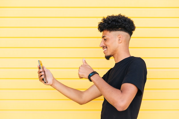 Cheerful ethnic male taking selfie with thumb up