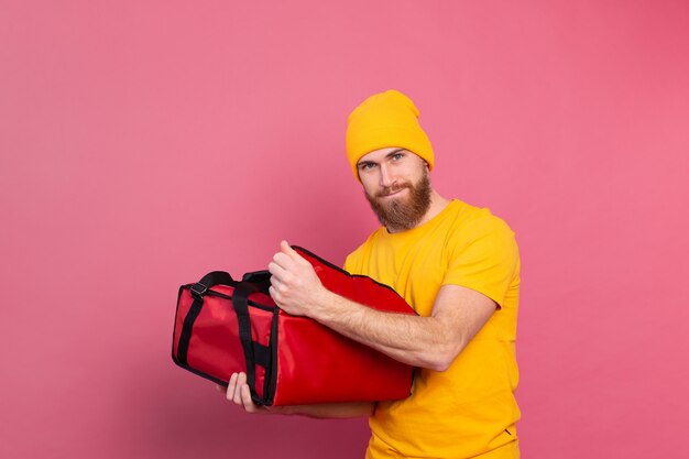 Cheerful european bearded delivery man surprised emotions open box with food on pink