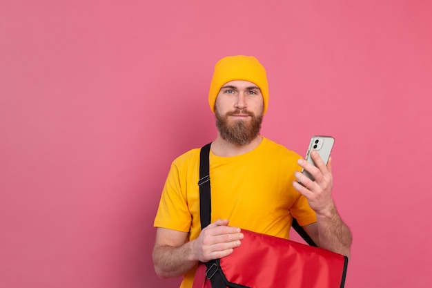 Cheerful european delivery man with bag casual hold phone on pink