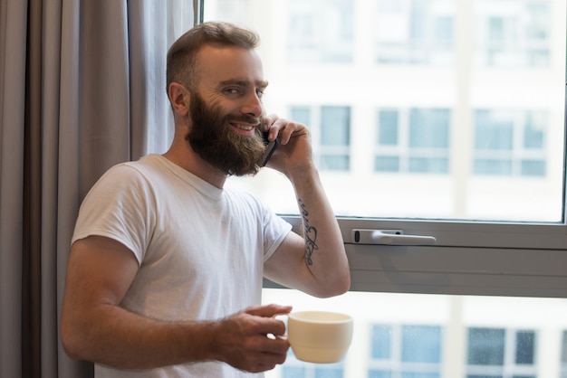 Cheerful excited man talking on phone while drinking coffee