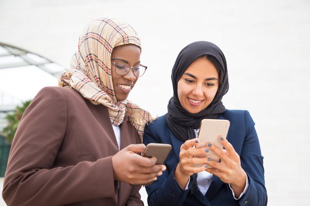 Cheerful excited office colleagues using smartphones