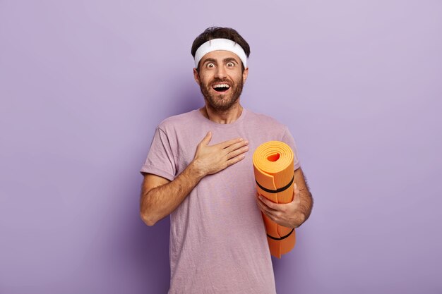 Cheerful excited sportsman looks with surprisement, touches chest, practices yoga every day