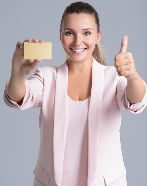 Cheerful excited surprised young woman with credit card and thumb up over white