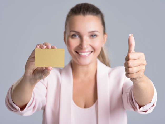 Cheerful excited surprised young woman with credit card and thumb up over white