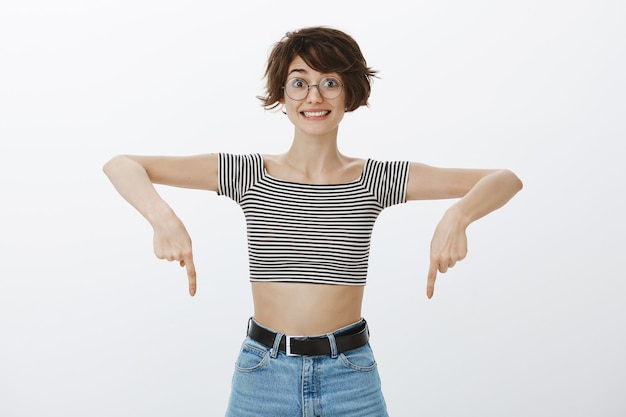 Cheerful excited woman looking upbeat while pointing fingers down