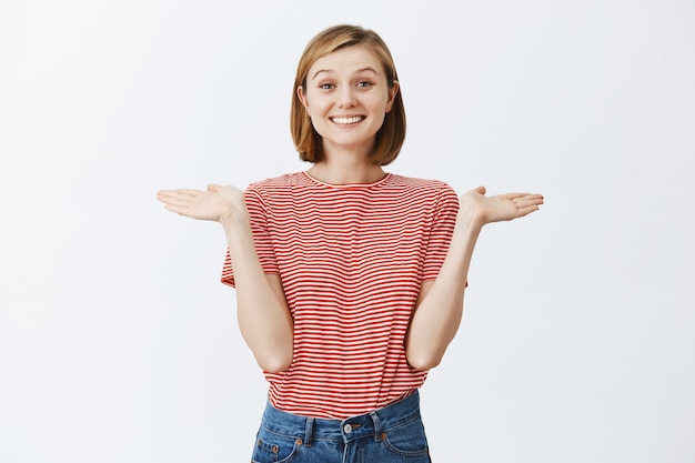 Foto gratuita giovane donna allegra ed eccitata che sembra felice, alzando le spalle con le mani allargate lateralmente