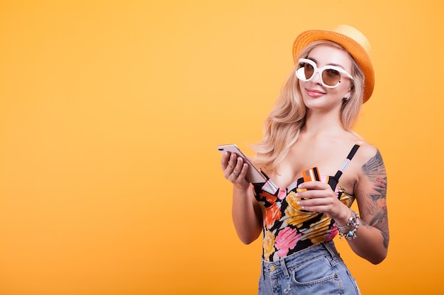 Cheerful excited young woman with mobile phone and credit card over yellow background