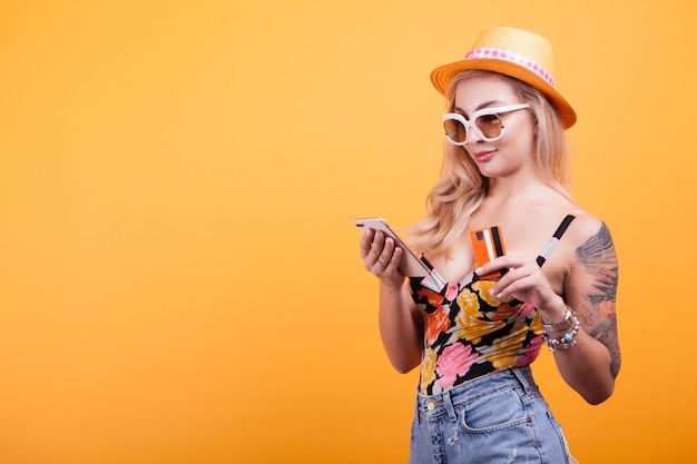 Cheerful excited young woman with mobile phone and credit card over yellow background