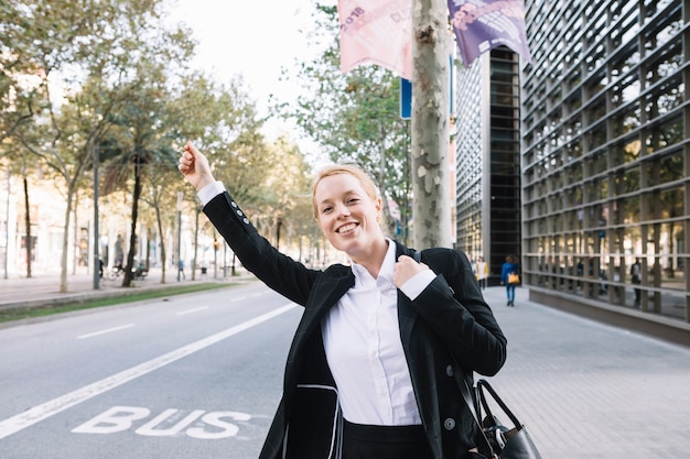 Cheerful executive in formal wear catching taxi on street