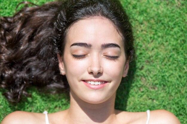 Cheerful face of young woman resting on grass