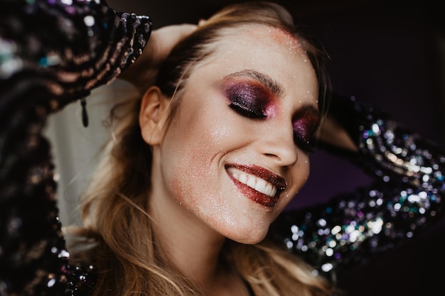 Free photo cheerful fairhaired girl laughing during fashion photoshoot studio portrait of amazing woman with dark purple makeup