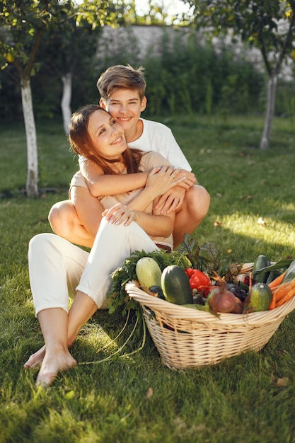 Cheerful family with organic vegetables in garden. Mixed organic vegetable in wicker basket. Mother with son in a backyard.