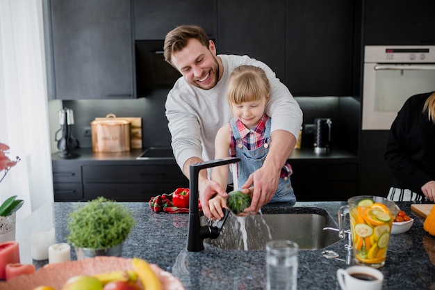 Cheerful father and daughter washing vegetables