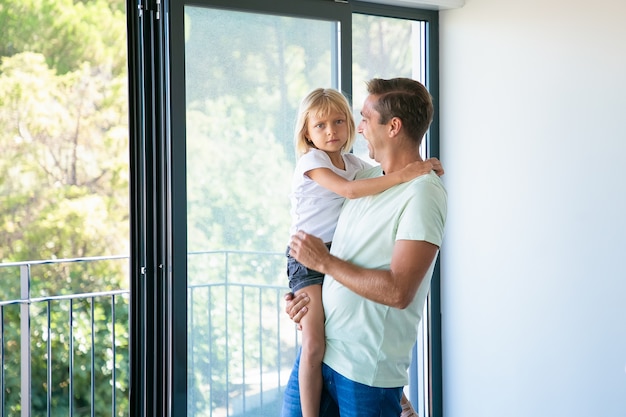 Cheerful father holding cute daughter, looking at her and smiling