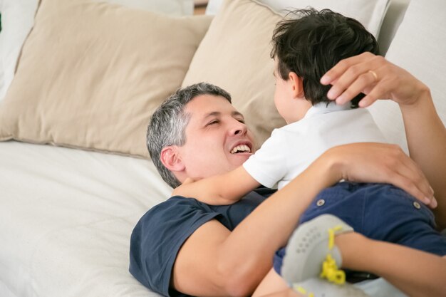 Cheerful father lying on sofa with adorable little boy.