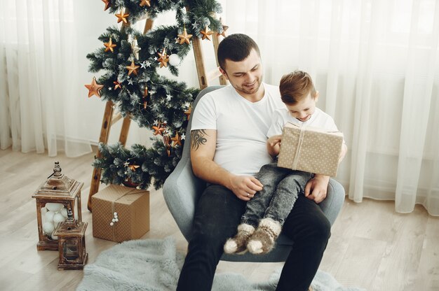 Cheerful father and son sitting near Christmas decorations. The boy is sitting with joy