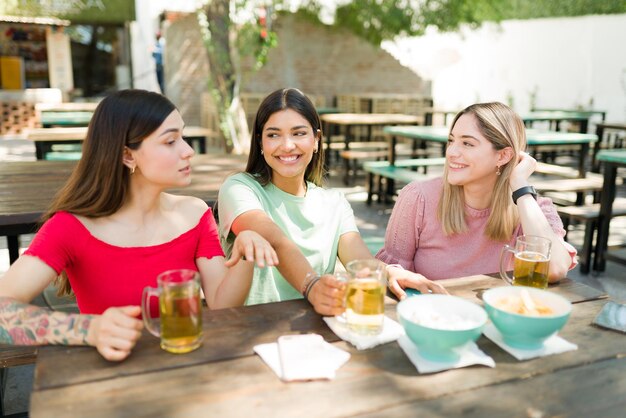 陽気な女性の親友がバーで飲み物を飲みながら話したりリラックスしたりします。いくつかのゴシップを共有し、一緒に冗談を言っている美しい多民族の女性