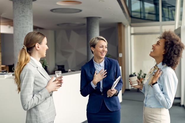 Cheerful female business colleagues having fun while talking in a hallway