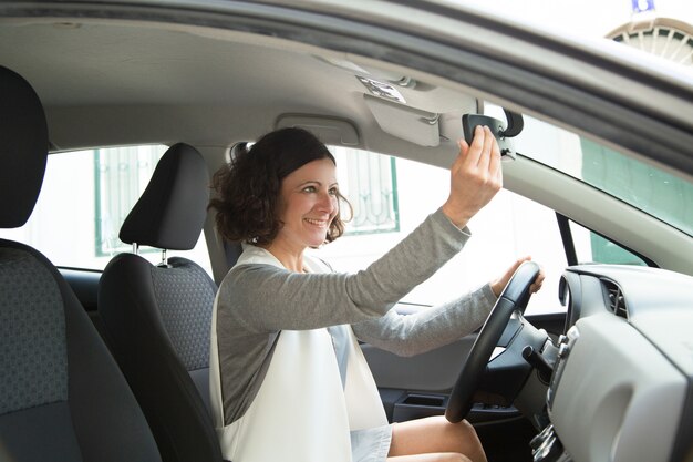 Cheerful female car driver looking in mirror