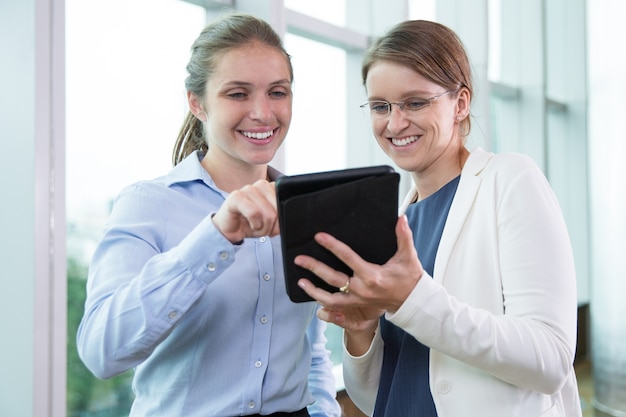 Cheerful female colleagues networking on touchpad