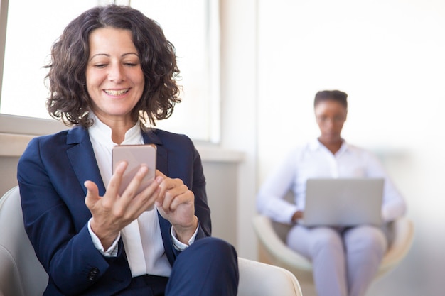 Free photo cheerful female employee watching content on cell