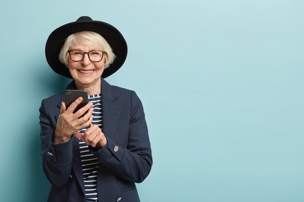 Cheerful female pensioner learns how to use smartphone, types notification