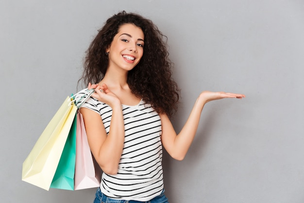 Cheerful female shopaholic being excited with all purchases and packs after shopping demonstrating product on her palm copy space