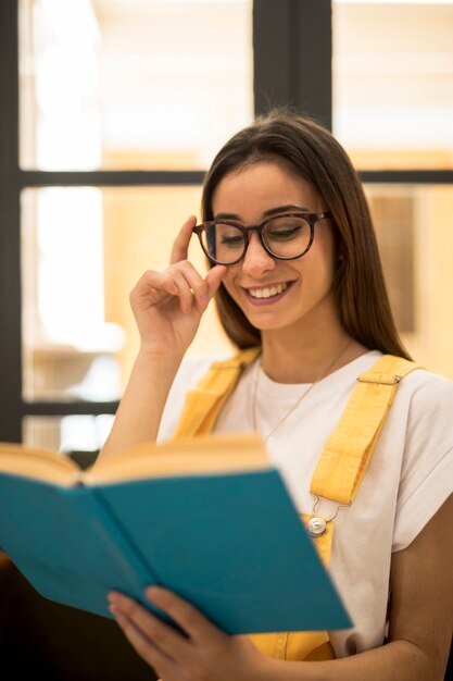 Веселая студентка читает книгу в очках