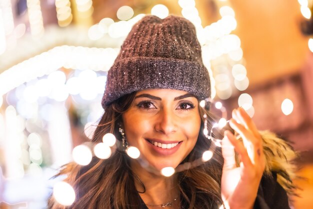 Cheerful female wearing a beanie and posing while holding Christmas lights outdoors